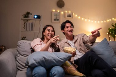 Asyalı genç ve güzel bir kadın evde romantik bir film izliyor. Çekici kız kanepede oturuyor, mutlu ve heyecanlı, dizide romantik komedi dizileri izliyor. Etkinlik yaşam tarzları konsepti.