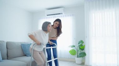 İçeride yürüyen yaşlı bir kadına yardım eden kadın.