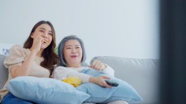 İki kadın birlikte televizyon izlerken abur cubur yiyor.