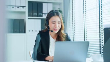 Kulaklık takan iş kadını ofiste dizüstü bilgisayarla çalışıyor.