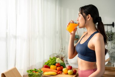 Spor giyimli Asyalı güzel bir kadın evde portakal suyu içiyor. Çekici genç spor kızı mutlu ve rahatlamış hissediyor, evde mutfaktaki sağlık hizmetleri için çalıştıktan sonra bir yudum sağlıklı içecek alıyor..