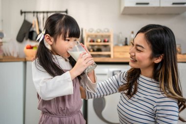 Asyalı küçük kız annesiyle mutfakta bir bardak süt içiyor. Çekici bir anne öğretmenlik yapıyor ve küçük kıza destek oluyor. Vücuduna iyi bakıyor. Evde sağlık hizmetleri için uyandıktan sonra süt içiyor..