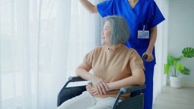 Hemşire tekerlekli sandalyedeki yaşlı kadına yardım ediyor.