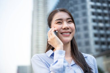 Asyalı genç iş kadını şehirde yürürken akıllı telefondan konuşuyor. Çekici, güzel bayan çalışan iş arkadaşlarıyla cep telefonlarında iletişim kuruyor ve yüksek binalarda iş arkadaşlarıyla tartışıyorlar..