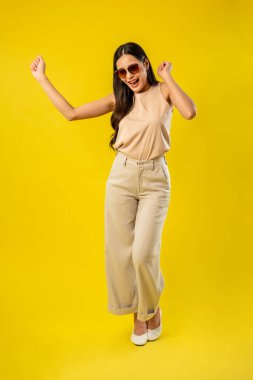 İzole edilmiş sarı arka planda duran Asyalı güzel bir kadının portresi. Çekici genç bayan model, stüdyo çekimlerinde poz verirken ve dans ederken kendine güvenerek gülümserken mutlu ve neşeli hissediyor.
