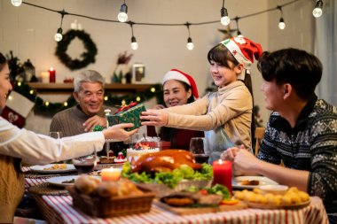 Asyalı sevimli aile evde Noel partisinde hediyelerini değiş tokuş ediyor. Bir grup çekici insan yemek masasında bayram kutlaması yaparken birbirlerinden hediye paketi alıyorlar.