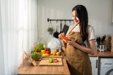 Asyalı genç bir kadın sabah evde mutfakta sağlıklı yemekler pişiriyor. Çekici kadın ev hanımı kendini mutlu ve rahat hissediyor, malzemeleri hazırlamaktan ve kahvaltıda yeşil salata yapmaktan hoşlanıyor..