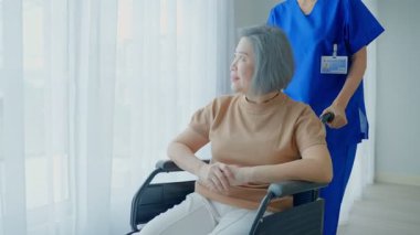 Tekerlekli sandalyede oturan yaşlı kadın bakıcısıyla içeride oturuyor..