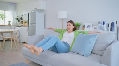Genç Asyalı mutlu kadın evdeki kanepede oturup dinleniyor..