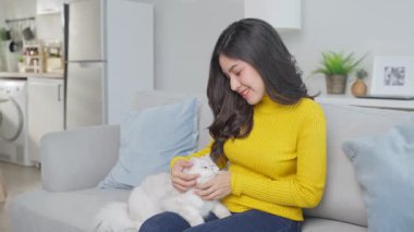 Uzun saçlı genç bir kadın beyaz kedisini içeride okşuyor..