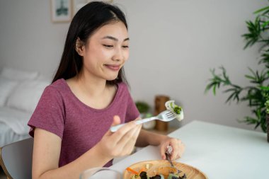 Asyalı genç bir kadın evdeki oturma odasında Vietnam böreği yiyor. Çekici, güzel bir kız masaya oturur, sabah evde sağlık için temiz aperatiflerin tadını çıkarır. Diyet ve Sağlıklı Yemek Konsepti