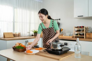 Asyalı genç bir kadın sabah evde mutfakta sağlıklı yemekler pişiriyor. Çekici kadın ev hanımı kendini mutlu hissediyor ve evde kahvaltıda çorba yapmak için malzemeler hazırlamaktan zevk alıyor..