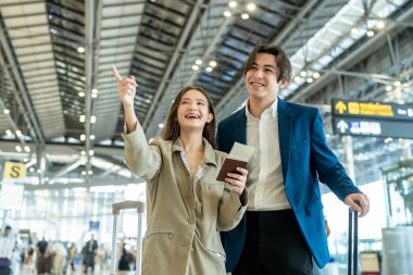 Asyalı işadamı ve kadın havaalanı terminalinden biniş kapısına doğru yürüyorlar. Çekici genç çift, tatil gezisi için uçakla yurtdışına giderken mutlu ve heyecanlı hissediyorlar..