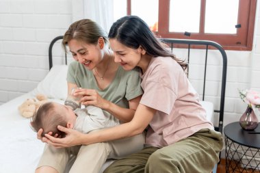 Asyalı lezbiyen çift, erkek çocuklarını evde büyütür ve büyütür. Süt şişesinden bebek besleyen iki kadın, sıcak aile ortamında çocuklarını beslerken hassas anlarını paylaşıyorlar..