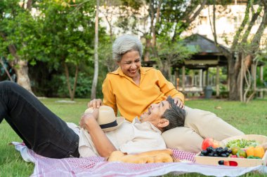 Asyalı yaşlı çift bahçede romantik bir randevuda vakit geçiriyor. Mutlu aile, çekici olgun erkek ve kadın neşeli ve rahat hissediyorlar gün batımında halka açık parkta piknik yapıyorlar.