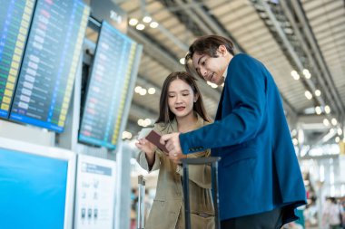 İş adamı ve kadın havaalanındaki uçuş çizelgesini kontrol ediyorlar. Çekici erkek ve kadın yolcular yurtdışına iş için gitmek için heyecanlı ve mutlu hissediyorlar..