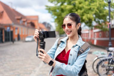 Asyalı kadın gezgin şehirde seyahat ederken kamera kaydı vlog 'u kullanır. Çekici bayan turist sokakta yürürken mutlu ve rahat hissediyor, Danimarka 'da tatil yaparken fotoğraf çekmenin keyfini çıkarıyor..