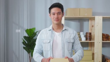 Asyalı genç adam gülümsüyor, elinde karton bir paket var..