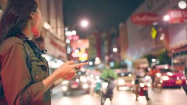Asyalı çekici kadın şehirde yürürken telefon kullanıyor. Güzel kadın turist, akıllı telefon kullanarak tek başına seyahat ediyor. Tatilde Tayland 'a tatile gidiyor..