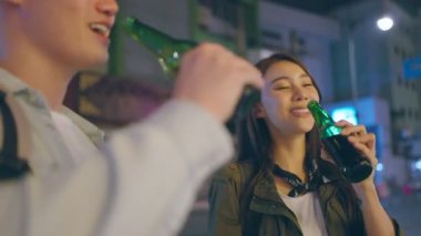 Asyalı çekici çift içki içiyor ve birlikte parti yapıyorlar. Genç adam ve kadın turistler şehirde tatilde birlikte vakit geçiriyorlar. Yol kenarında gecenin karanlığında ellerinde bira şişeleriyle..