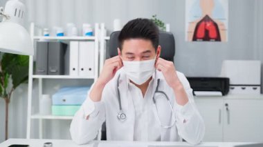 Asyalı doktor tıbbi ofiste koruyucu yüz maskesi ayarlıyor..