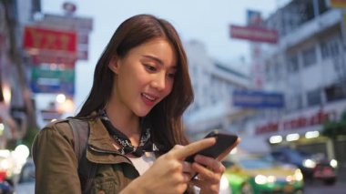 Dışarıda akıllı telefon kullanırken gülümseyen genç bir kadın.