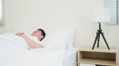 Genç Asyalı adam rahat beyaz bir yatakta mışıl mışıl uyuyor..