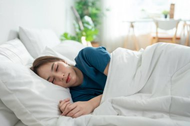 Asyalı güzel bir kadın sabahları yatak odasında yatağa uzanıyor. Çekici genç kız kendini mutlu ve rahat hissediyor, rahat bir yastık ve battaniyeyle uyuyor tatilde hafta sonunun keyfini çıkarıyor..