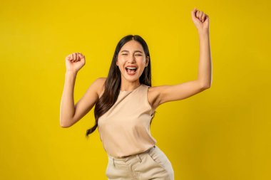 İzole edilmiş sarı arka planda duran Asyalı güzel bir kadının portresi. Çekici genç bayan model, stüdyo çekimlerinde poz verirken ve dans ederken kendine güvenerek gülümserken mutlu ve neşeli hissediyor.