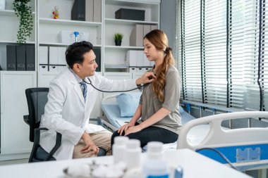 Asyalı kardiyolog hastanedeki kalp atışı olan hastayı dinledi. Sağlık hizmetleri kliniğindeki randevusu sırasında hasta kadını tedavi etmek için çalışan profesyonel bir doktor..
