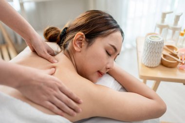 Asyalı genç bir kadın güzellik merkezinde sırt masajı yaptırıyor. Çekici, güzel bir kız masaj yatağında uzanıyor ve masaj salonundaki vücut için masözden rahatlatıcı fizyoterapi hizmeti alıyor.