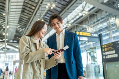 Asyalı işadamı ve kadın havaalanı terminalinden biniş kapısına doğru yürüyorlar. Çekici genç çift, tatil gezisi için uçakla yurtdışına giderken mutlu ve heyecanlı hissediyorlar..