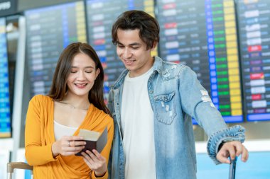 Havaalanındaki uçuş tarifesini kontrol eden Asyalı yolcular. Çekici genç turist arkadaşları tatil için ayrılış terminaline uçakla gitmekten mutlu ve heyecanlı hissediyorlar..