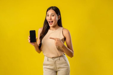 İzole edilmiş sarı arka planda akıllı telefonu tutan Asyalı kadının portresi. Çekici genç kız manken stüdyo ekranında çevrimiçi dijital cep telefonu aygıtı kullanırken mutlu ve neşeli hisseder..