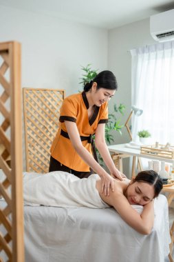 Asyalı genç bir kadın güzellik merkezinde sırt masajı yaptırıyor. Çekici, güzel bir kız masaj yatağında uzanıyor ve masaj salonundaki vücut için masözden rahatlatıcı fizyoterapi hizmeti alıyor.