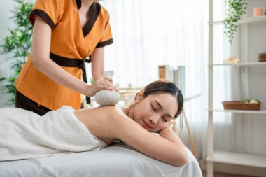Asyalı genç bir kadın bitkisel poşetlerle Tayland masajı yaptırıyor. Çekici, güzel bir kız masaj yatağında uzanıp masaj salonundaki masözden rahatlatıcı fizyoterapi hizmeti alıyor..