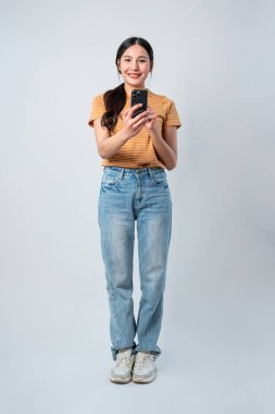 Gri arka planda cep telefonu tutan Asyalı güzel bir kadın. Çekici genç kız model mutlu ve neşeli hissederken Stüdyo ekran çekiminde çevrimiçi dijital akıllı telefon aygıtı kullanılıyor