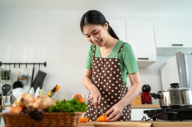 Asyalı genç bir kadın sabah evde mutfakta sağlıklı yemekler pişiriyor. Çekici kadın ev hanımı kendini mutlu hissediyor ve evde kahvaltıda çorba yapmak için malzemeler hazırlamaktan zevk alıyor..