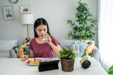 Asyalı genç bir kadın evdeki oturma odasında Amerikan kahvaltısı yiyor. Çekici kız masaya oturur, sabahları evde sağlık için temiz suyla İngiliz kahvaltısı yapar. Diyet ve Sağlıklı Yemek Konsepti.