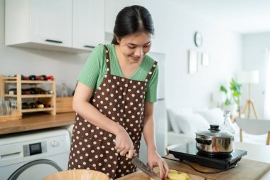 Asyalı genç bir kadın sabah evde mutfakta sağlıklı yemekler pişiriyor. Çekici kadın ev hanımı kendini mutlu hissediyor ve evde kahvaltıda çorba yapmak için malzemeler hazırlamaktan zevk alıyor..