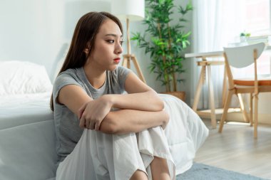 Depresyondaki Asyalı kadın yatak odasında yerde tek başına otururken üzülüyor. Çekici, hayal kırıklığına uğramış, üzgün ve başı ağrıyan bir kız. Sağlık hizmetleri İfadesi.