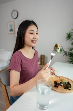 Asyalı genç bir kadın evdeki oturma odasında Vietnam böreği yiyor. Çekici, güzel bir kız masaya oturur, sabah evde sağlık için temiz aperatiflerin tadını çıkarır. Diyet ve Sağlıklı Yemek Konsepti