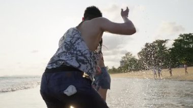 Gün batımında sahilde su sıçratan genç yetişkinler..