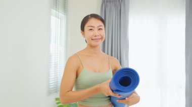 Asyalı mutlu kadın odada yoga minderi tutuyor..