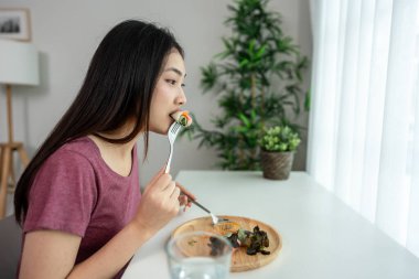 Asyalı genç bir kadın evdeki oturma odasında Vietnam böreği yiyor. Çekici, güzel bir kız masaya oturur, sabah evde sağlık için temiz aperatiflerin tadını çıkarır. Diyet ve Sağlıklı Yemek Konsepti