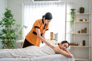 Asyalı genç bir kadın güzellik merkezinde sırt masajı yaptırıyor. Çekici, güzel bir kız masaj yatağında uzanıyor ve masaj salonundaki vücut için masözden rahatlatıcı fizyoterapi hizmeti alıyor.