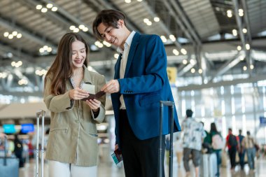 Asyalı işadamı ve kadın havaalanından kalkış biletini kontrol ediyor. Çekici erkek ve kadın yolcu tatil gezisi için uçakla yurtdışına gittikleri için mutlu ve heyecanlı hissediyorlar..