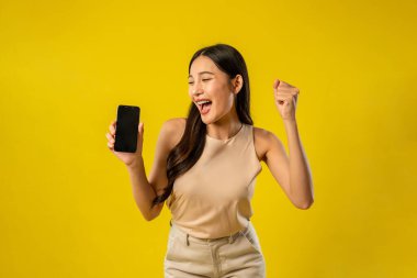 İzole edilmiş sarı arka planda akıllı telefonu tutan Asyalı kadının portresi. Çekici genç kız manken stüdyo ekranında çevrimiçi dijital cep telefonu aygıtı kullanırken mutlu ve neşeli hisseder..
