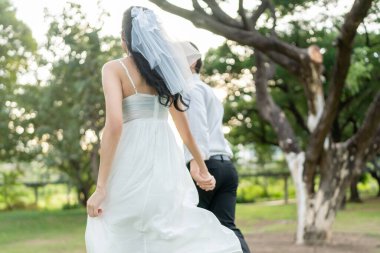 Gün batımında parkta el ele tutuşan Asyalı genç bir çift. Çekici romantik damat ve gelin koşuyor, aşklarını ve sevgililer gününü kutluyorlar, düğün öncesi dışarıda eğleniyorlar..