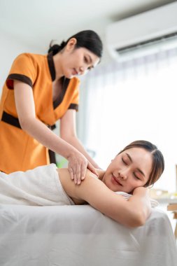 Asyalı genç bir kadın güzellik merkezinde sırt masajı yaptırıyor. Çekici, güzel bir kız masaj yatağında uzanıyor ve masaj salonundaki vücut için masözden rahatlatıcı fizyoterapi hizmeti alıyor.